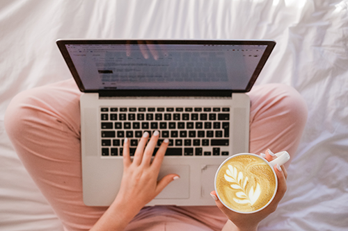 خانمی در حال نوشیدن قهوه و کار با لپ تاپ